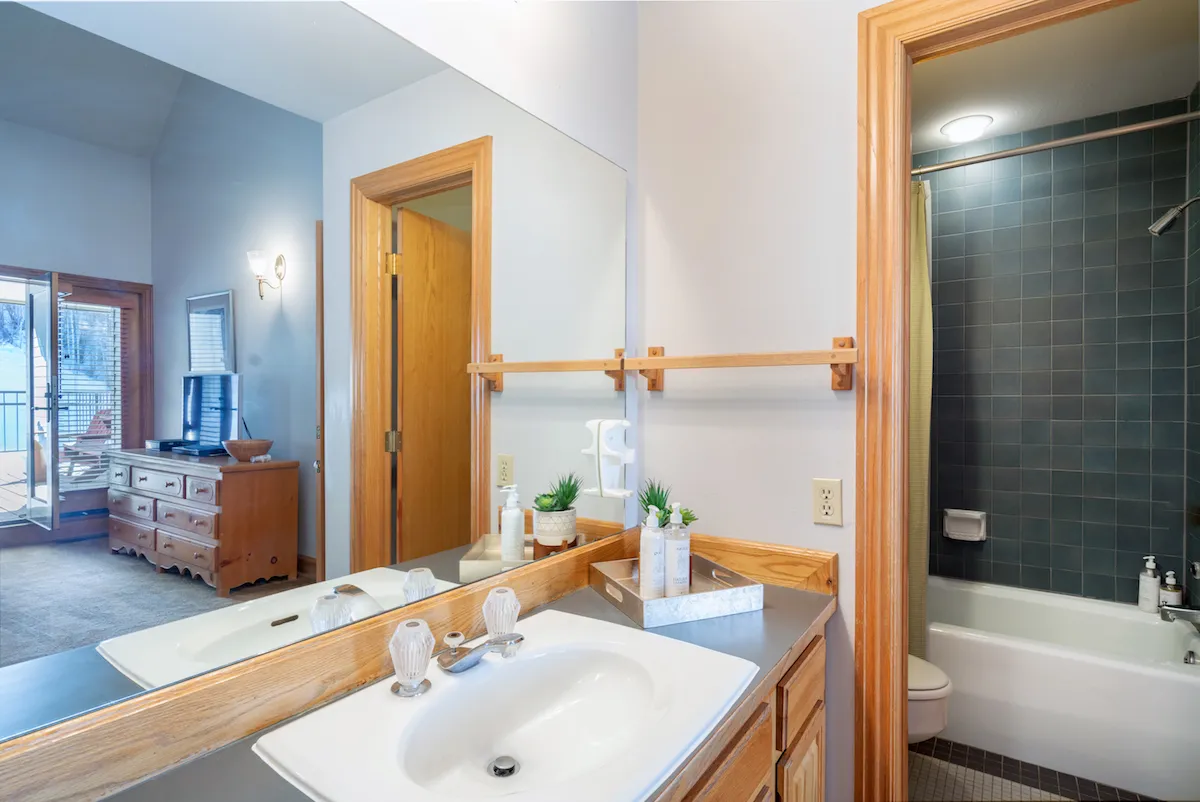 A well-appointed bathroom with a large vanity, wooden cabinetry, a spacious mirror, a shower area in the background, and touches of greenery for a spa-like feel. The organized and calming setup makes it ideal for refreshing after a mountain adventure.