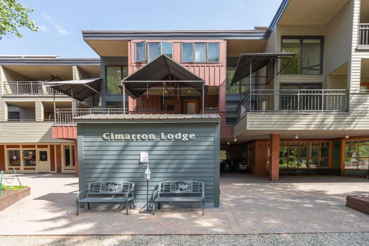 The exterior of Cimarron Lodge features a welcoming sign, comfortable benches, and architectural details beneath canopies. The area is designed for relaxation, with spaces that encourage guests to sit, socialize, or enjoy coffee in the fresh mountain air.