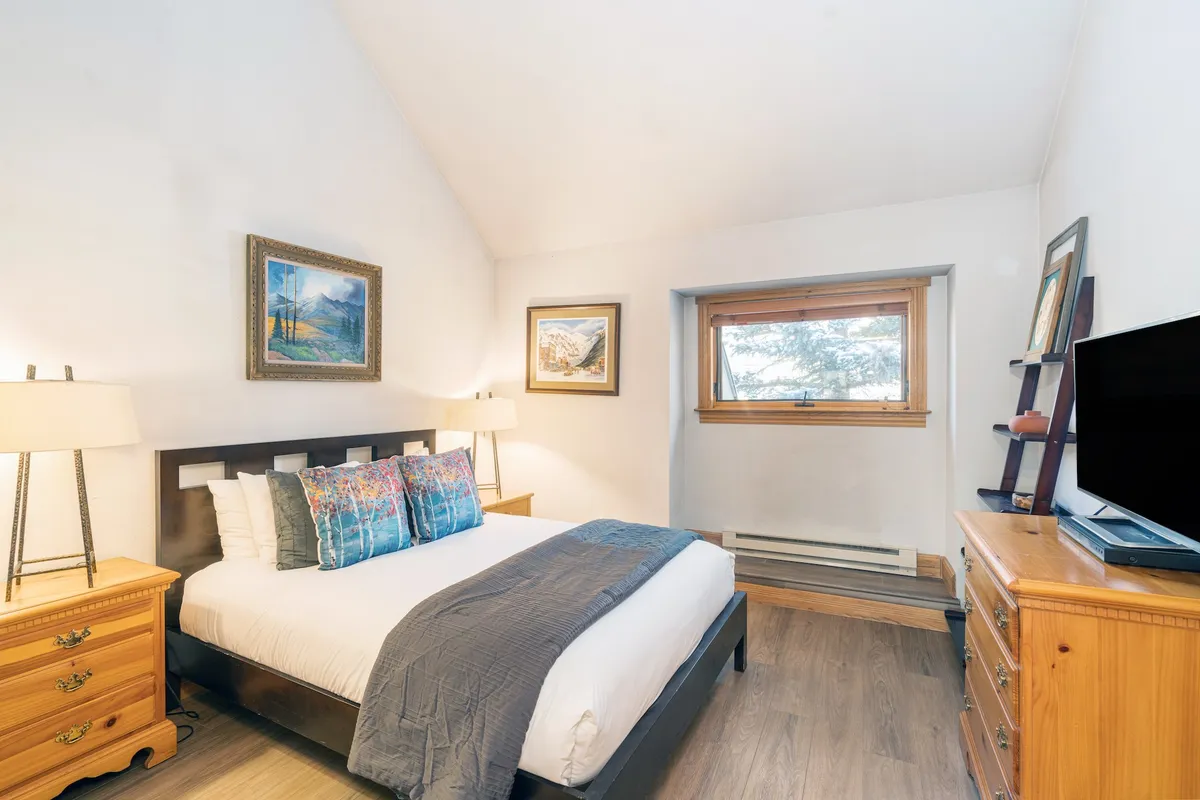 A serene queen bedroom with a comfortable bed, tasteful artwork, nightstands, and a television. The room exudes warmth and is perfectly suited for guests seeking privacy and relaxation.