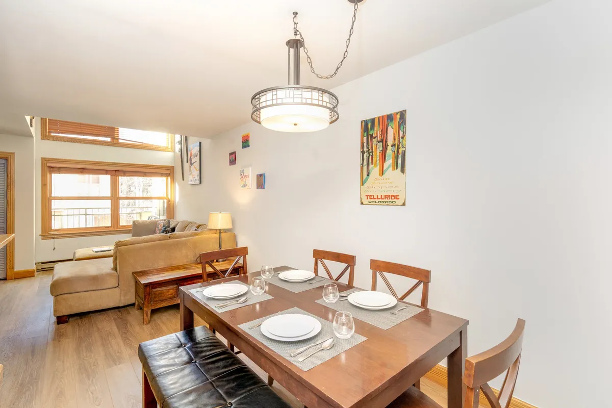 An inviting open-concept area featuring a dining table set for a meal, a comfortable couch nearby, and decorative wall art. Sunlight pours in, highlighting the communal space that's perfect for family dinners, game nights, or casual gatherings after a day outdoors.