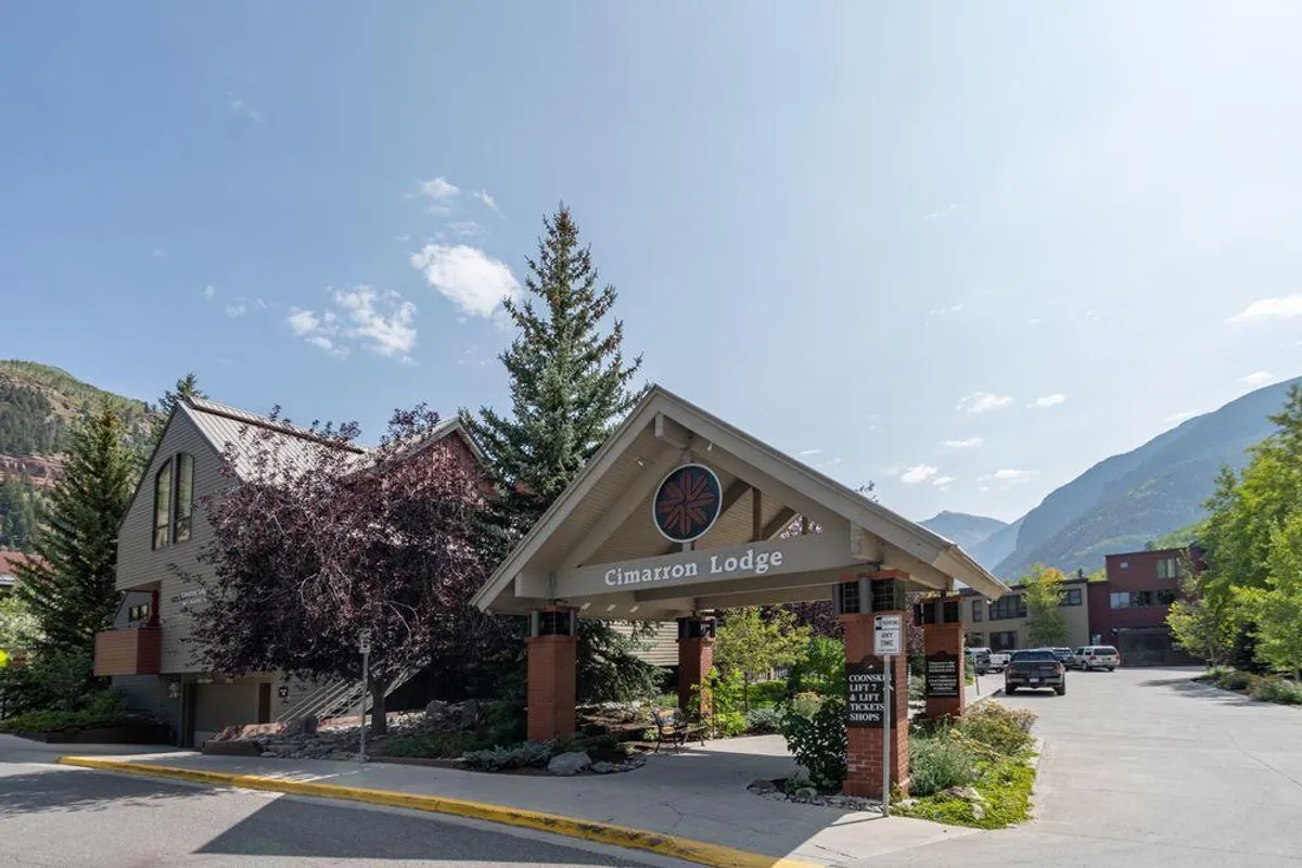 The welcoming entrance to Cimarron Lodge is framed by trees and an entrance canopy, with the lodge sign clearly visible. Mountains fill the background, highlighting Telluride’s beautiful natural setting and the property’s inviting, serene atmosphere.