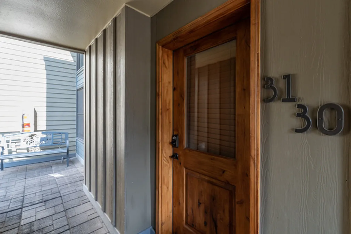 A welcoming exterior entryway featuring a wooden door marked with the unit number, textured walls, and a cozy bench for sitting. This image conveys a sense of arrival and comfort, highlighting the ease of access and the building’s inviting character.